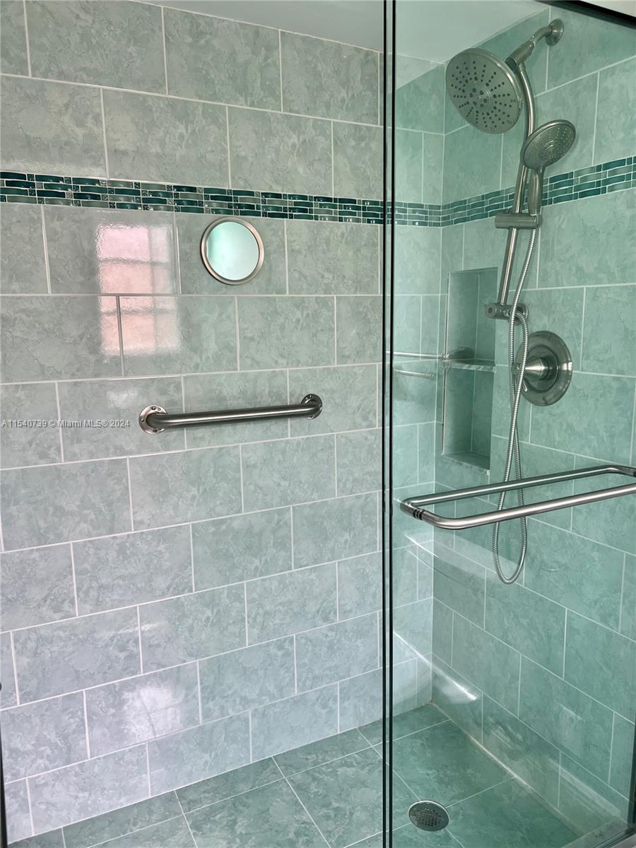 Updated primary walk-in shower featuring beautiful tile work, glass tile border and grab bar.