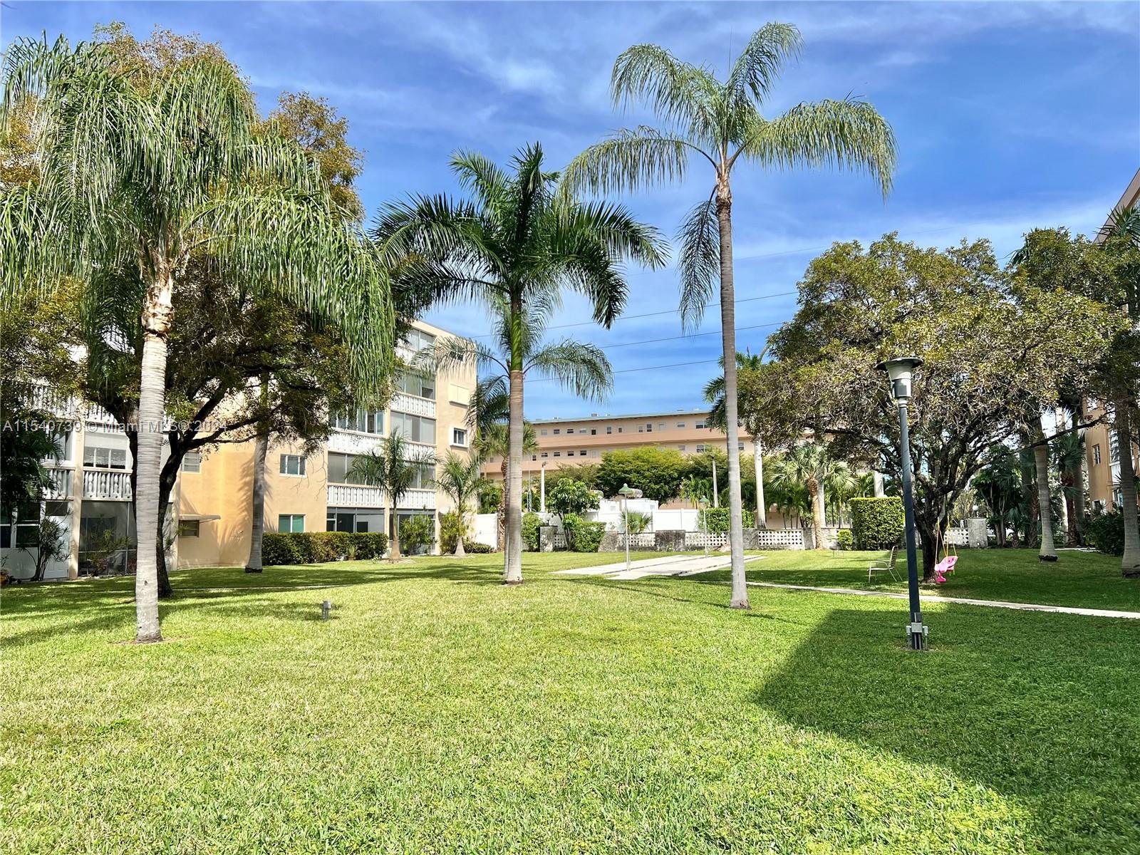 Expansive green courtyard. Mature trees and palm trees.