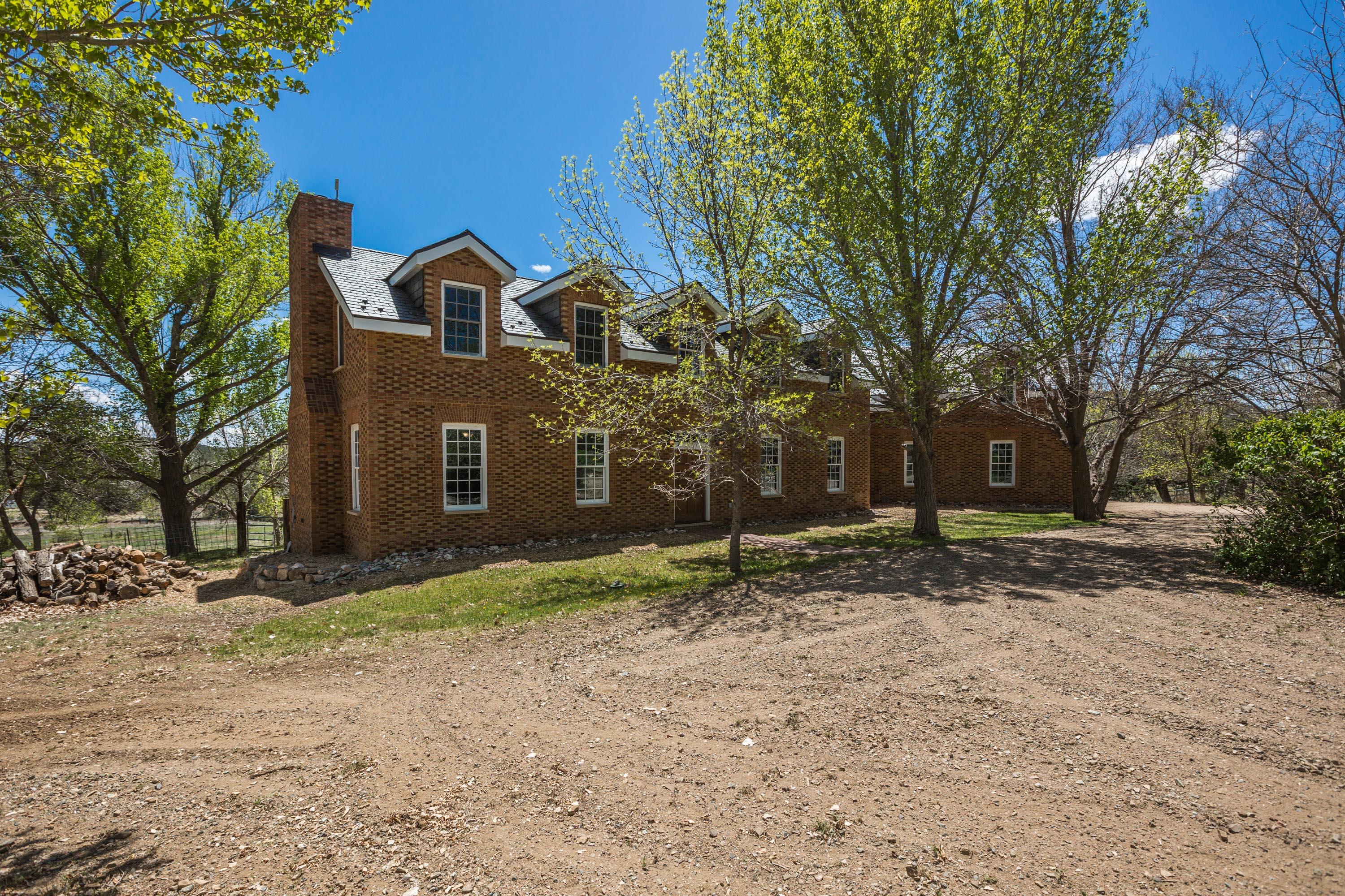 Unique opportunity to own an amazing part of New Mexico's scenic beauty while enjoying the comforts of a thoughtfully designed home. The gated driveway conceals the treasures within, offering privacy and seclusion. This remarkable property on 27.7 acres offers many possibilities, whether you envision it as a horse property, a farm, or your own private retreat. Custom-built 7000sq ft Colonial Williamsburg home with Virginia brick exterior enhances timeless elegance. Pitched roof with 500-year slate tiles, ensuring durability and a classic look. Tennessee walnut kitchen cabinets and soapstone countertops. Solid red oak flooring throughout the home. The property boasts abundant water resources, including 40 acre-feet of owned irrigation rights and 3 good wells, to supply ample water, making