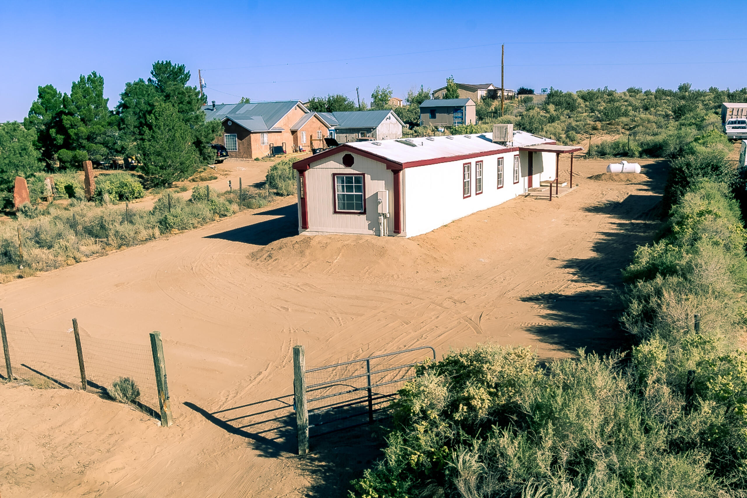 Single-wide on a half-acre on a paved road with City water but located in the County. Fenced and gated. Good floorplan with separated primary suite complete with full bath and walk-in closet. Two more bedrooms in front share a full bath. Large living room + eat-in kitchen with built-in china cabinet. Laundry room with additional storage. Refrigerator, washer and dryer all convey. East-facing covered porch + west-facing covered deck. Recent propane water heater.