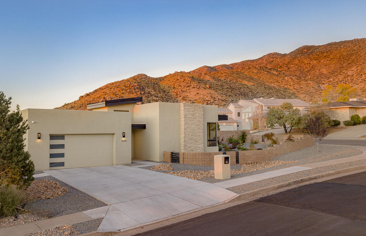 Nestled in the foothills at the end of Indian School Rd, this stunning 2022 Las Ventanas home combines style and sophistication. East-facing windows flood the space with natural light and showcase breathtaking views of the Sandia Mountains. The gourmet kitchen, designed for entertaining, features smart technology and high-end finishes. Art-specific lighting highlights the home's curated interior, while motorized window coverings are controlled via a Wi-Fi hub. The spacious main ensuite includes a luxurious wet/dressing area, large walk-in closet, and private patio. A second ensuite offers accessibility features. Smart home systems control security, climate, privacy, and more.  Steps away from hiking and mountain biking enhance this exceptional lifestyle.