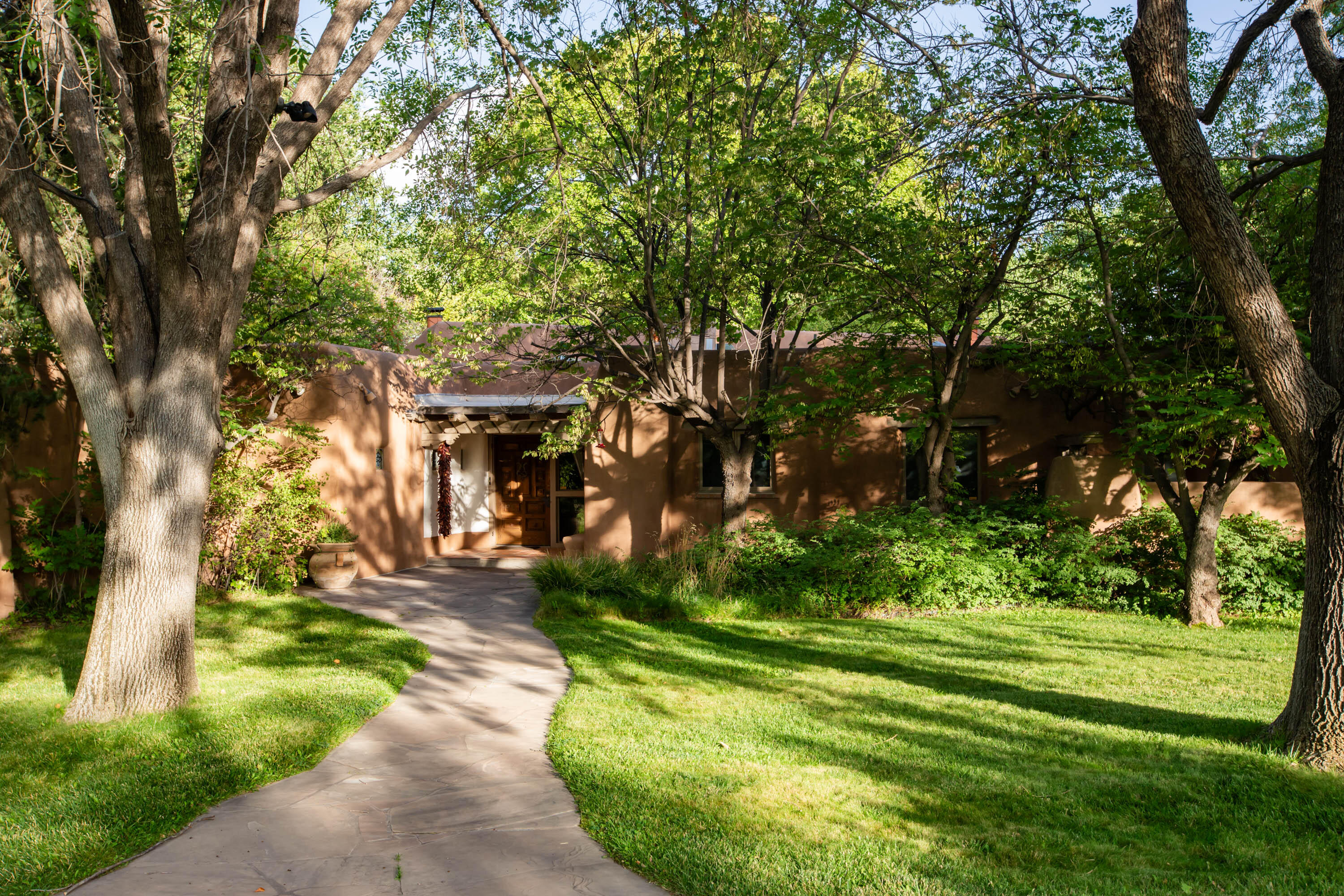 The essence of New Mexican adobe architecture located in the lush coveted Los Poblanos Estates near the Rio Grande in the Village of Los Ranchos.The soft sculptural walls envelope you with a peaceful vibe. The home was built in 1984 by famed adobe builder, Nat Kaplan. Sited on 3.34 acres, privacy is abundant. Short distance to Los Poblanos Inn. Recently renovated, the home has a newer roof, updated kitchen and baths, renovated pool, and a sports court. Connected to city water and sewer, the home also has a private irrigation well and ditch irrigation. The apple orchard has 20+ trees. The home has 3 spacious bedrooms all on one level. The large den could also serve as a 2nd primary bedroom with its own entrance. Gated entry to the property ensures privacy.