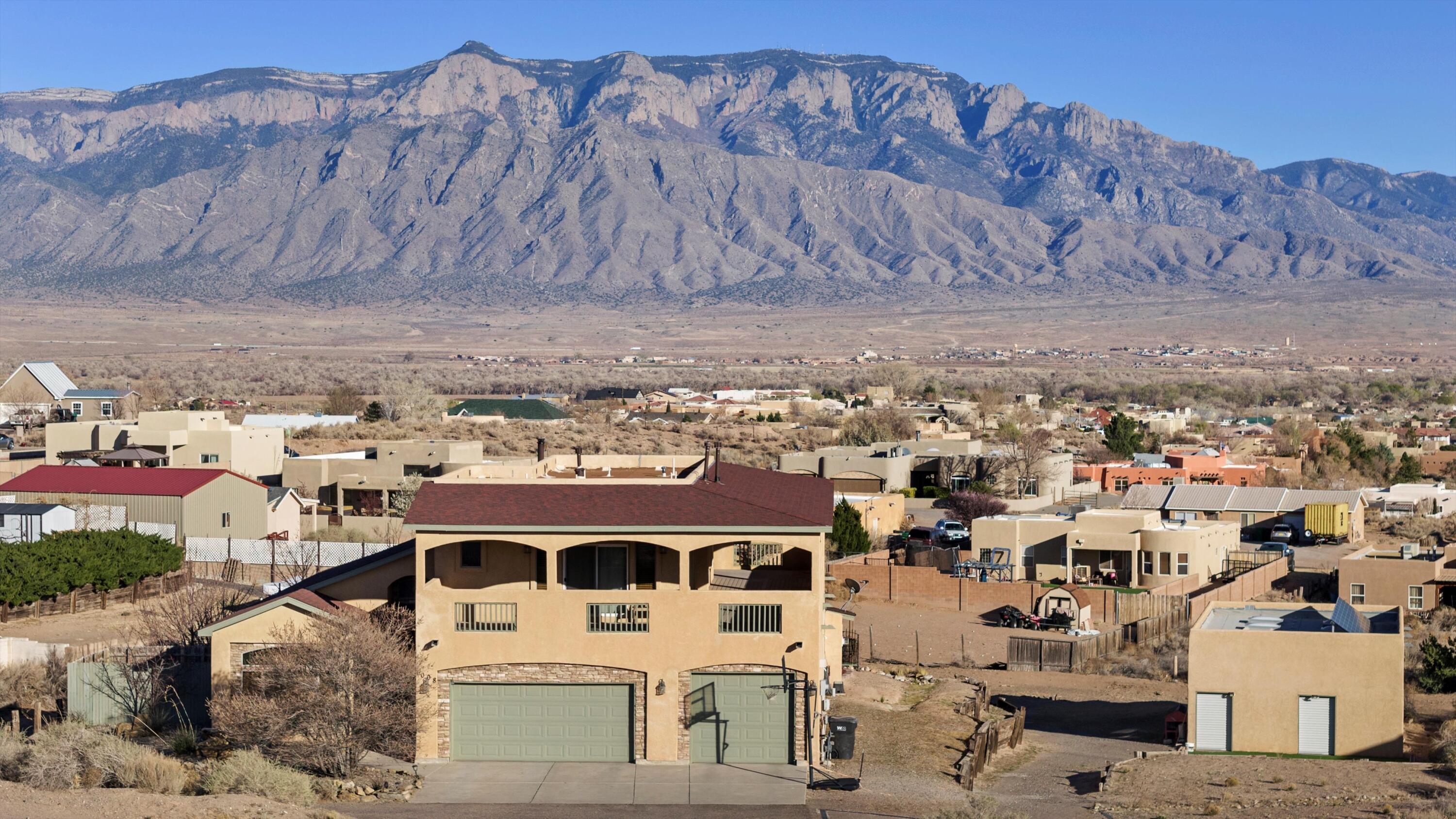 Welcome to this exquisite two-story residence, offering 4 bedrooms, 4 bathrooms, and an attached 3.5-car garage, complemented by an additional detached 2-car garage/man cave.  Situated on nearly an acre of land, this home boasts a full wraparound deck, providing breathtaking views of the city lights and the stunning Sandia Mountains.  Designed with an open-concept floor plan, the home features two primary suites, one of which includes a luxurious soaking tub, a separate shower, and a versatile bonus room--ideal for a home office, gym, or hobby space.   With two units for heating and cooling plus indoor and outdoor fireplaces, you are sure to stay comfortable all year round.  Enjoy outdoor living at its finest on the expansive back patio, perfect for relaxation and entertaining.