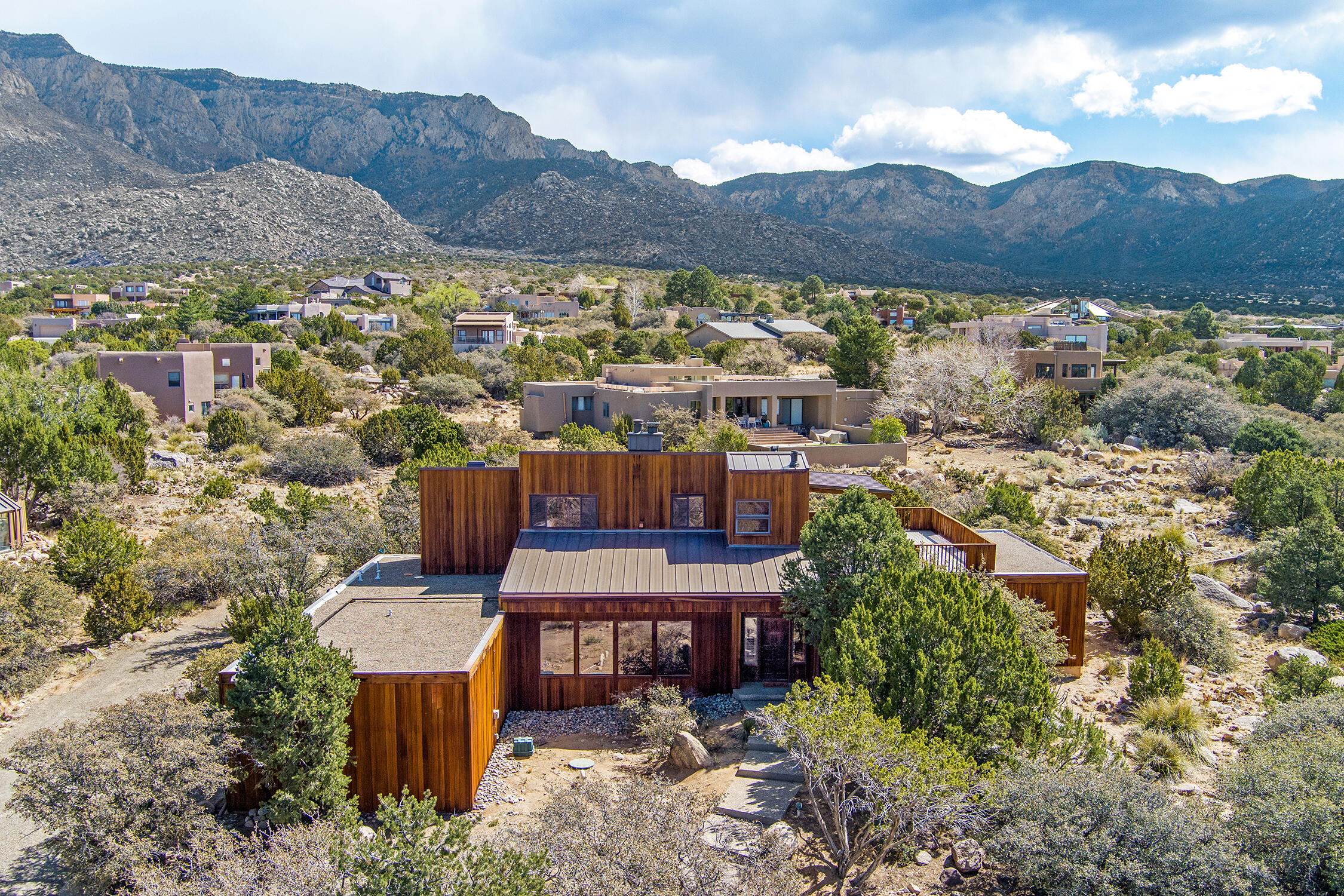 Sandia Heights dream home! Custom-built w/ sensational views of the mountain range and valley, sense of privacy on 3/4 acre lot. Warm and inviting w/ beautiful redwood siding, raised ceilings, Saltillo tiles, and premium wood shutters. Bright, kitchen/dining, granite counters, maple cabinetry, counter seating, lots of storage, mountain vista. Primary bedroom suite w/ huge walk-in closet, fireplace, bahroom suite, access to enormous trex deck w/ premier views. Three more spacious bedrooms on main floor, plus flex room serves as an office/2nd living space. Spa w/ hot tub, sauna, bathroom. Garage workshop space. Refrigerated air, 2 units. NEW metal roof main home & NEW gutters (2025), re-finished floor ducts (2025), new garage roof (2019), new 50 gal water heater, new upgraded septic (2022).