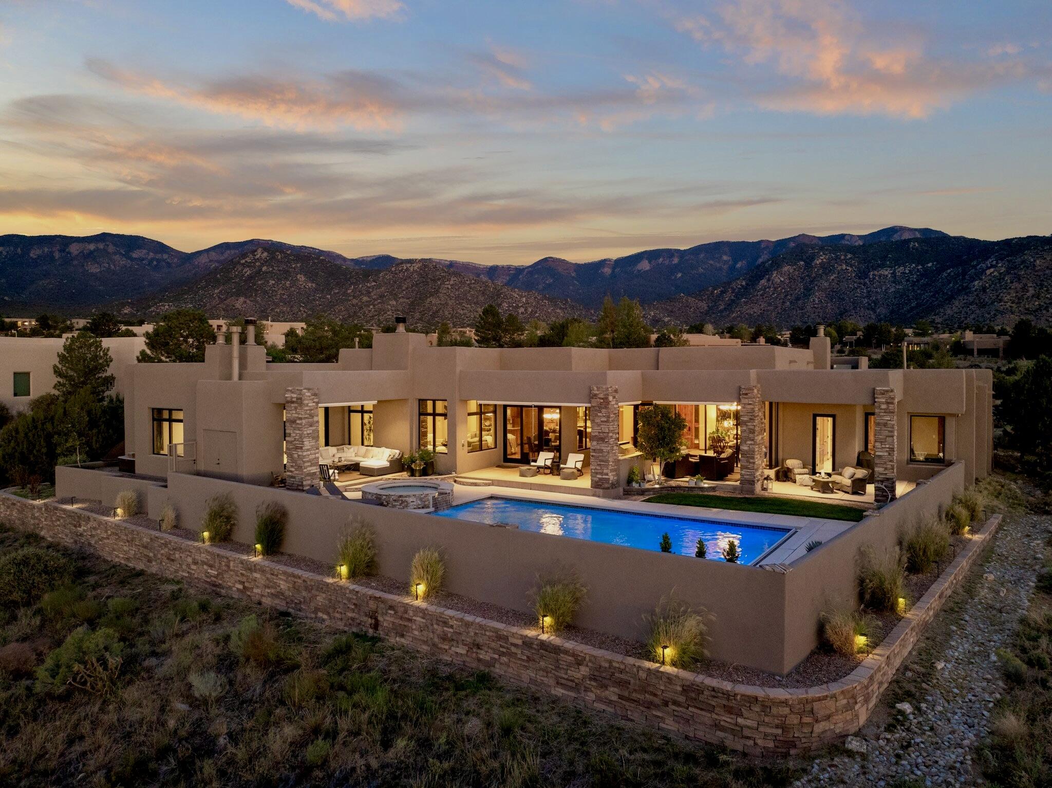 Contemporary and elegant, this stunning home is positioned perfectly to enjoy unobstructed views of the sunsets, city lights, and Sandia Mtns. Courtyard entry invites you into this light-filled home with flowing floor plan and seamless living between indoor & outdoor spaces. Entertainer's dream kitchen!  Plenty of workspace, 3 ovens, 2 dishwashers, Wolf range, lrg pantry & Subzero fridge. Stylish living spaces divide the North & South wings. Spectacular primary suite on North wing includes sitting area & fireplace where one enjoys moments of reflection overlooking open space below or city lights beyond. South wing with 2-3 bdrms (1 w/en-suite), generous closets & office w/ amazing views. Media room w/bar & recreation area. Salt water pool, hot-tub, covered patio, outdoor living area!