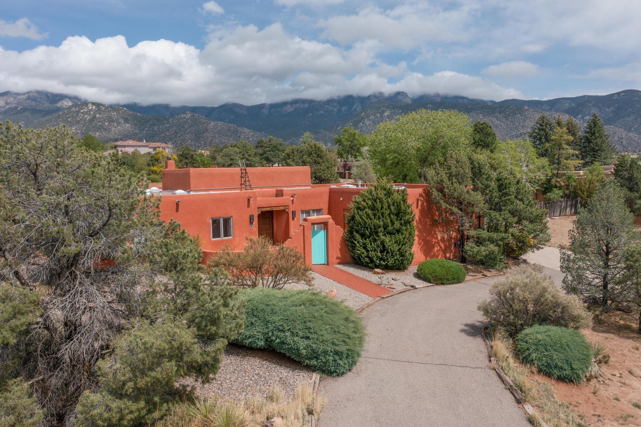 Nestled in Sandia Heights, this charming home boasts unobstructed views of the Sandia's & is beautifully enveloped by desert landscaping.Step through the inviting front courtyard & discover a residence filled w/SW charm. The expansive living room features striking wood beams, traditional kiva fireplace, & clerestory windows that fill the space with natural light. Elegant window pane French doors offer stunning views of the mountains. Kitchen includes a comfortable breakfast area,adjacent dining room provides an ideal setting for entertaining. Spacious owner's suite offers a relaxing reading area,complete w/ built-in bookcases & a unique two-way kiva fireplace. This thoughtfully designed layout also includes 3 additional bedrooms. Enjoy the sunrises & sunsets from your covered porch patio.