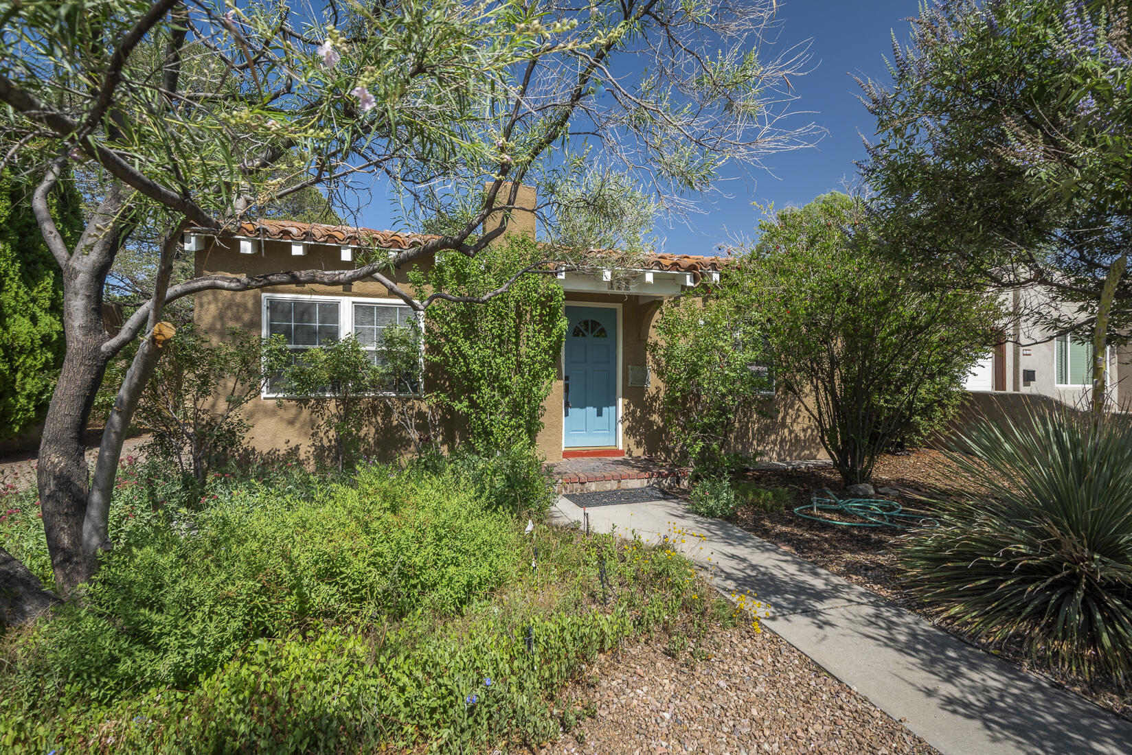 A distinctive Nob Hill bungalow with lots of charm and character! Located in the heart of the very popular College View neighborhood! One level with hardwood floors, coved ceilings, decorative fireplace and other vintage touches. Living and dining rooms. Kitchen with saltillo tile floor. (Full-size and mini fridges convey.) Two bedrooms. One full bathroom awash in colorful tile! Separate workshop/storage (100 sqft) with washer and dryer and NEW water heater (June 2025). Detached one-car garage. Huge fenced backyard with kiva fireplace, flagstone patio and blooming mimosa! Easy access to Nob Hill, UNM, law/med schools, Downtown and golf.