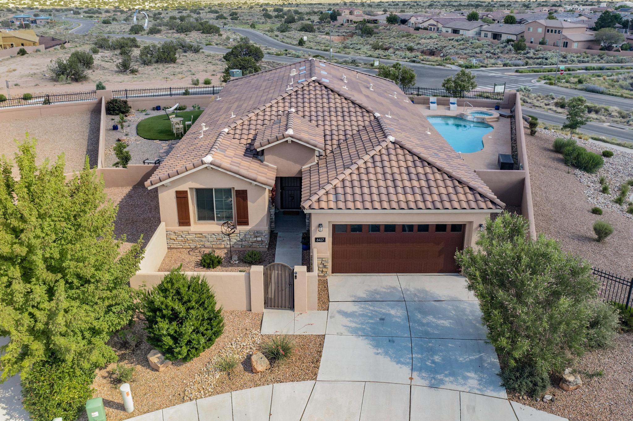 Gorgeous single-story home on an elevated lot in gated Mariposa with stunning city and Sandia views! Designed for outdoor living with a Heated POOL, HOT TUB, kiva fireplace, turf w/ sprinklers, and oversized covered patio w/ auto shades. Courtyard entry with custom gate sets the tone. Wood-look tile throughout, open-concept layout, cozy fireplace, built-in office, and flex room. Gourmet kitchen with granite counters, backsplash, and built-in appliances. Spacious primary suite with soaker tub, walk-in shower, and large closet. Rare lot offering exceptional privacy!