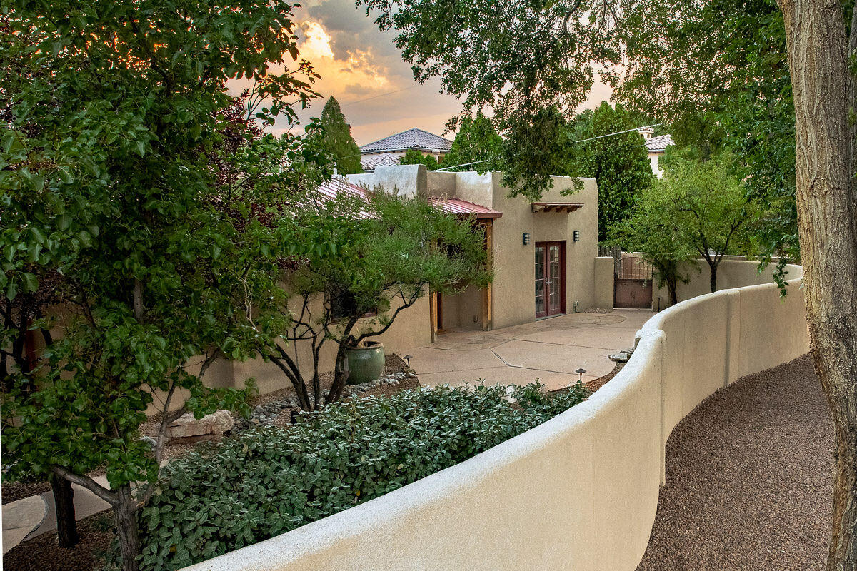 Tucked behind an adobe wall and lush landscaping, this exceptional property blends historic charm with modern comfort. Originally built in 1933 and expanded in 2007 by an award-winning builder, the home features reclaimed imported doors, artisan tilework, and unique architectural details. The kitchen was updated in 2020, with recent upgrades including new TPO roofing and an added HVAC unit. The luxurious primary suite offers dual baths, a snail shower, jetted tub, fireplace, and walk-in closet. A detached casita includes a full kitchen, living area, bedroom, bath, laundry, and private garage. The park-like yard features mature trees, lush grass, multiple courtyards, and a well-fed irrigation system, offering privacy and tranquility.