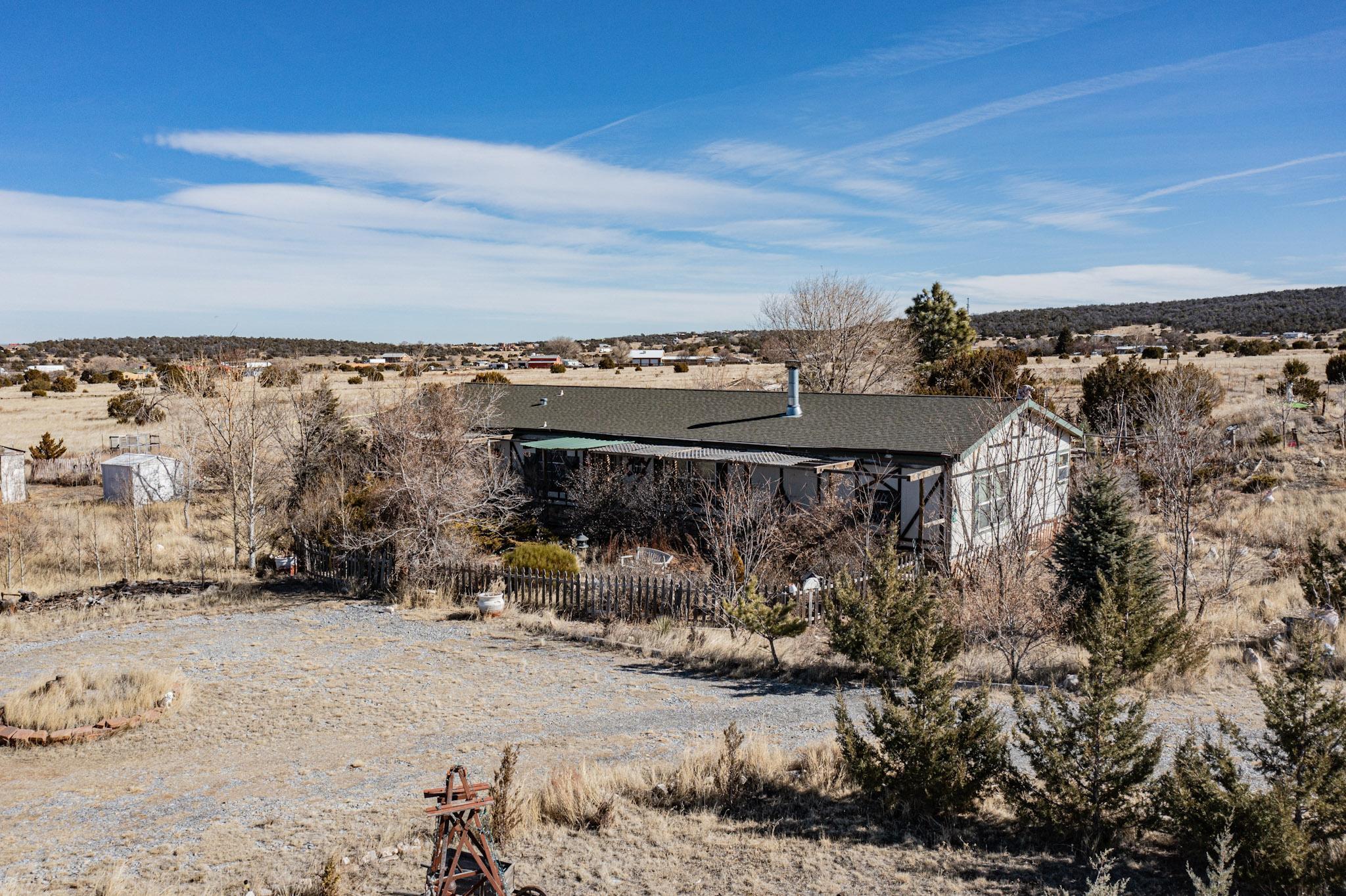 What an amazing find! This 2,361 square foot, 3 bed, 2 bath home sits on 11.54 beautiful and private acres of land, just 20 short minutes from Albuquerque. Large kitchen with ample storage, a huge primary bedroom suite, two living areas with a double sided fireplace, and a large laundry room with a water softener and chest freezer. Owned solar panels! Outbuilding has covered parking for your car or RV, as well as storage or workshop space on either side. Both areas have power, and one side is insulated as well. Approximately 2.25 acres are fully fenced and wonderfully landscaped. This property is covered with well established trees, as well as flowering shrubs and bushes. There is a kilometer long walking path around the property where you will not be bothered or disturbed.