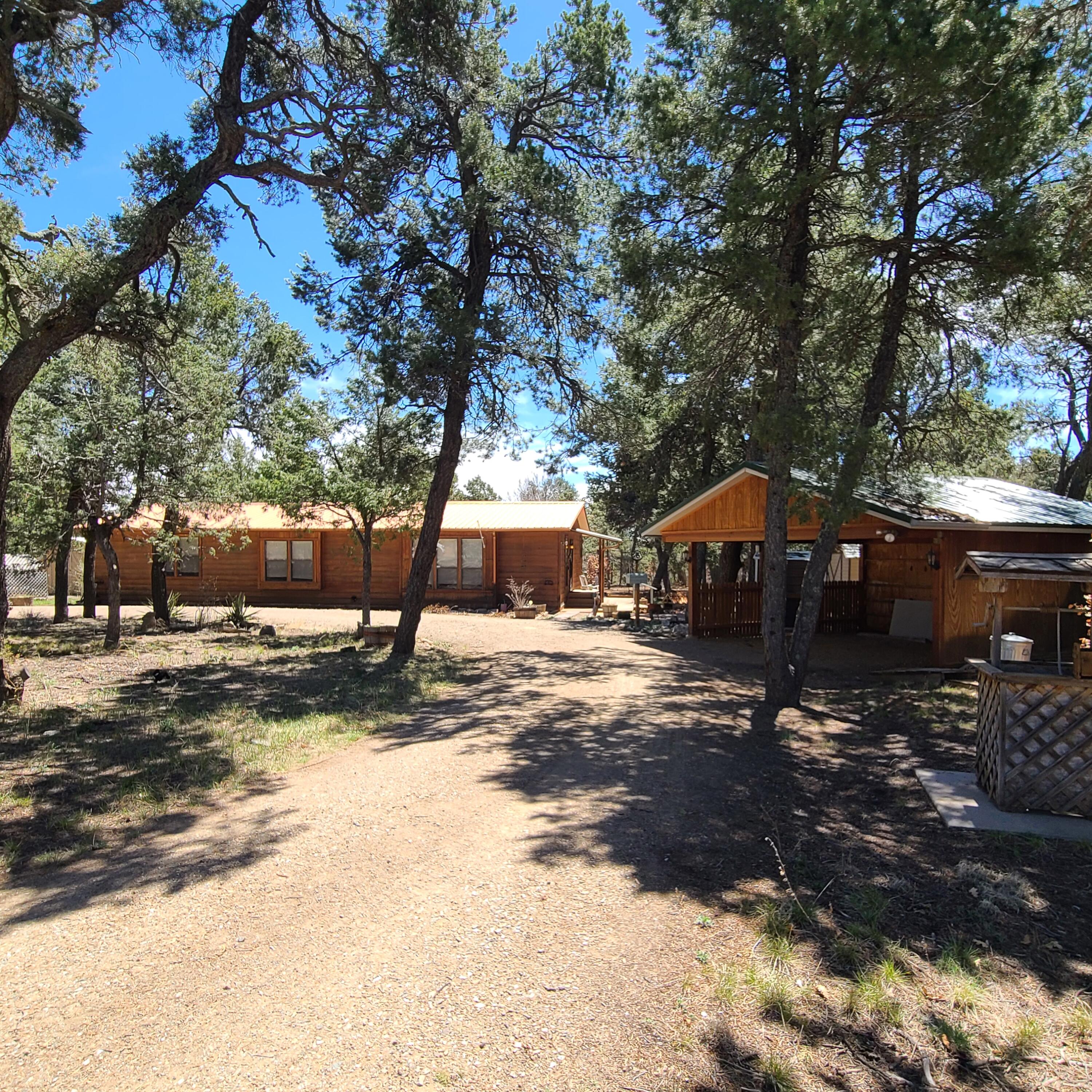 Welcome to Paradise! No traffic, 2 acres serene greenery w/ pines, cedars, pinons, oaks! Nestled in the trees, private retreat been dreaming about. Single level, 3 bed with poss 4th, 2 bathrms, no carpet, spacious! 2 car carport, multiple sheds, workshop w/ power, greenhouse, RV pad with dump sump & power. Walk in to high ceilings, open plan, lg windows. Living rm has wood burning FP, 2 dining areas/flex space. Spacious kitchen w/ gas stove, 2 pantries, corner windows. Down the hall 3 bedrms, spare full bath, storage, coat closet. Primary is large, any size furn will fit. 2 closets, 2 sink vanity, large walk in shower, storage, window with a view. Bonus 4th bedrm/office/flex rm with door to BY deck. NEW septic drain field, furnace, water heater, roof resealed, exterior getting sealed. GEM