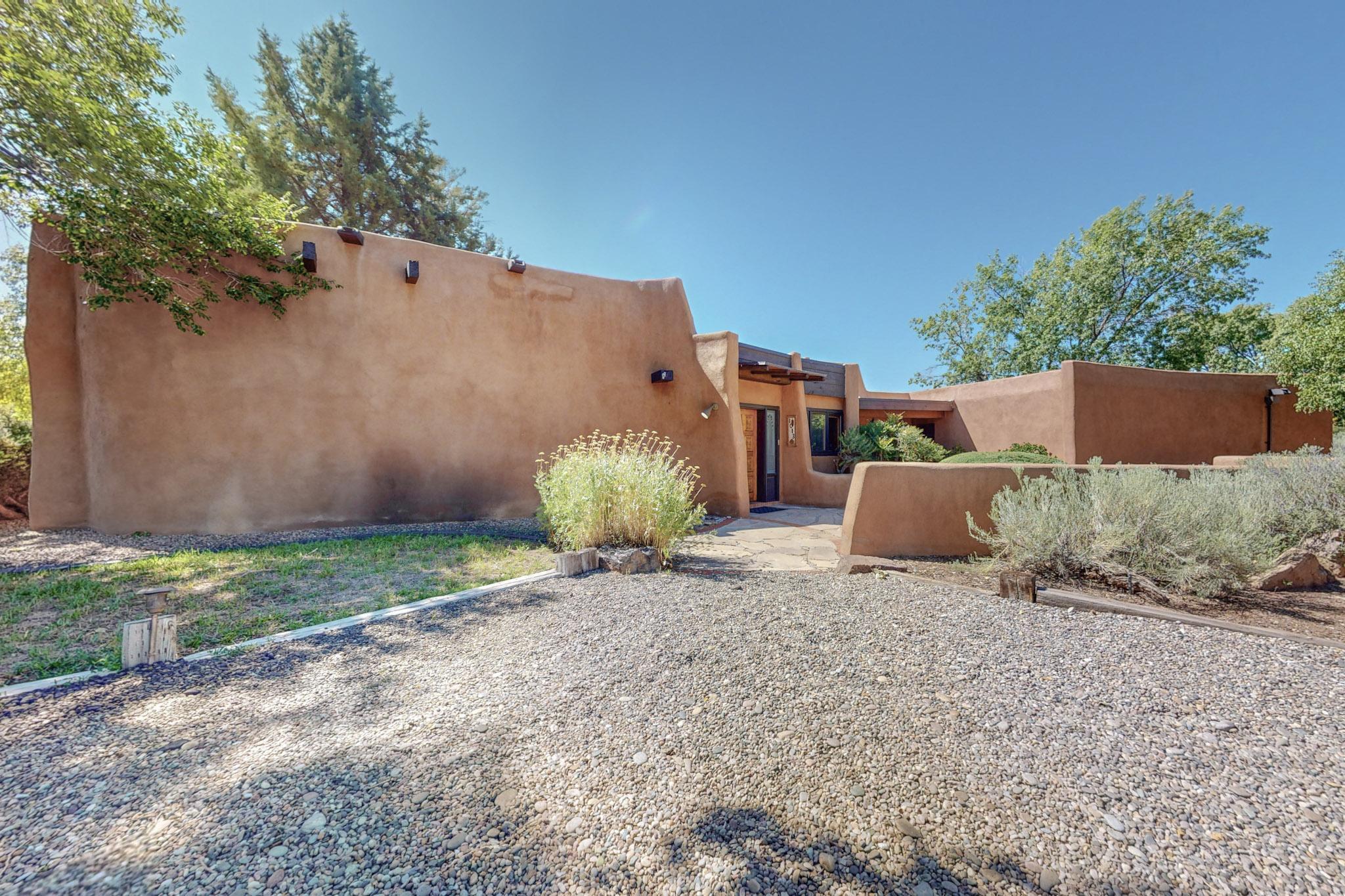 Custom adobe home with beautiful brick floors, nichos, bancos, pony walls, and a stunning dual adobe fireplace, cathedral beam ceilings, and owned solar. Updated gourmet kitchen is a chef's dream, with abundant granite counter space and plenty of efficient cabinetry, including convenient pull-out shelves. Spacious Primary wing includes a cozy sitting room/office, elegantly separated by an adobe pony wall. Hallway windows on the opposite two-bedroom wing offer passive solar heat, creating a warm and inviting atmosphere during the cool winter months. This wonderful property is nestled near the Rio Grande River amidst lush grapevines and wineries in the charming El Caballero Norte neighborhood with access to Hartnett Park's tennis courts and Grower's Market.